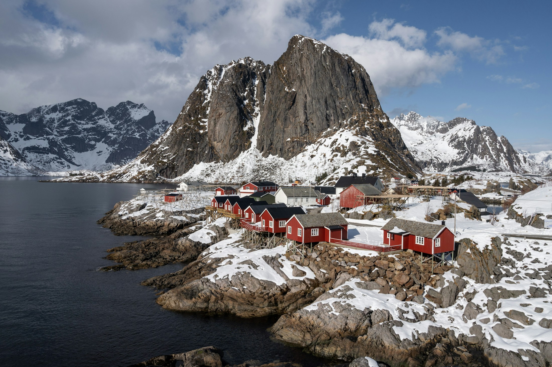 Red fishing cabins beside the sea and snowy mountains in Lofoten